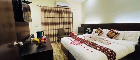 Habitación de hotel con cama, escritorio, silla, ventilador de techo, aire acondicionado y ventana con cortinas.