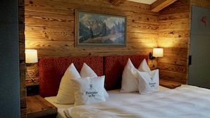Habitación con paneles de madera, una cama y un cabecero tapizado en rojo, además de dos lámparas fijadas a la pared.