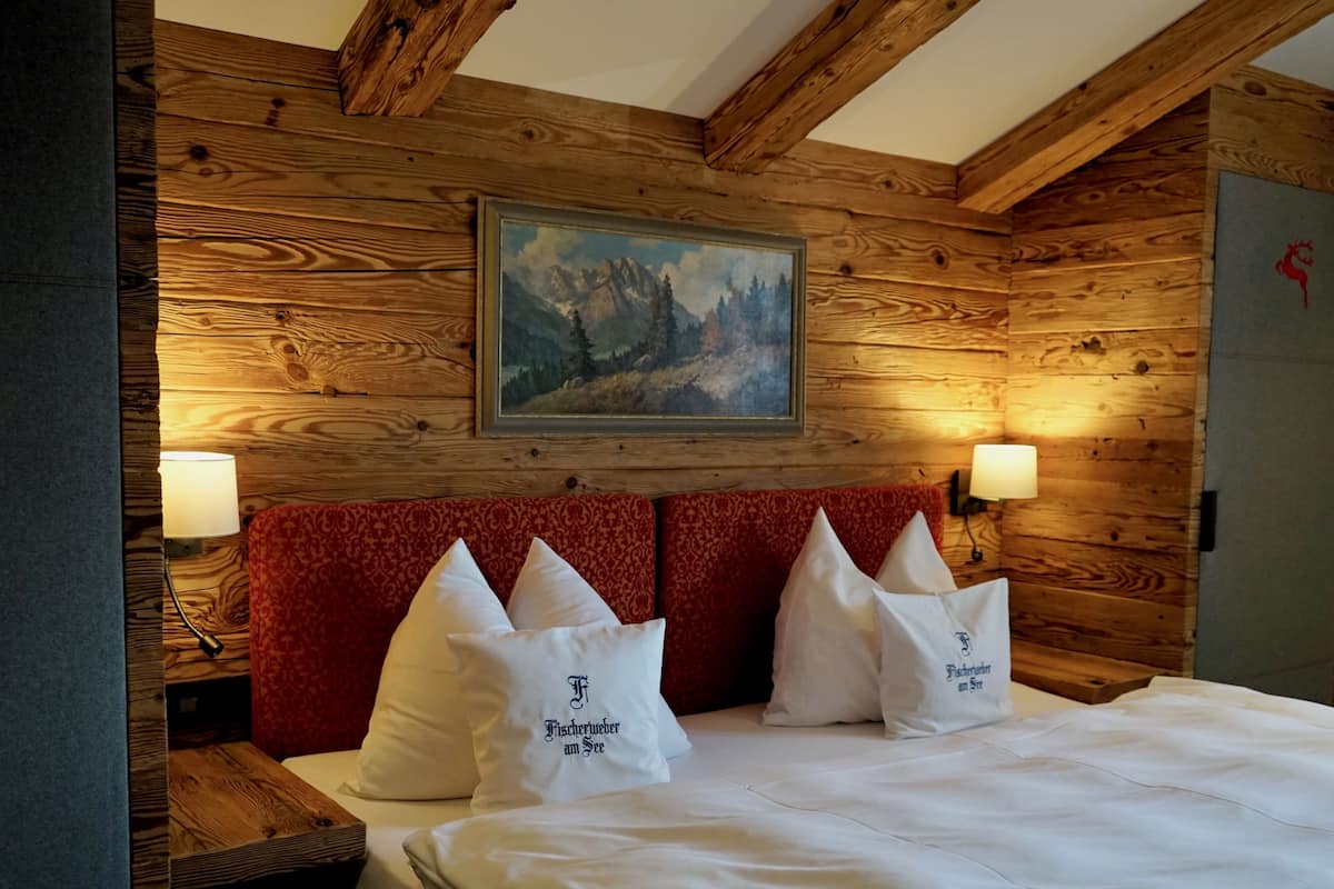 Una stanza con rivestimento in legno, un letto e un poggiatesta imbottito di rosso, illuminata da due lampade fissate al muro.