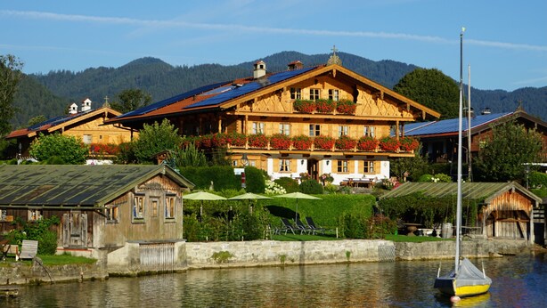 Un edificio de madera con balcón, un velero y montañas al fondo.