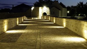 A paved pathway leading to a stone building with a central archway, surrounded by walls and illuminated by artificial lighting. - Kata Peaceful Apartment (Nin)