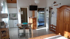 A bedroom with a bed, a desk with two chairs, a television, and a kitchen area with cabinets and a sink. - Kata Peaceful Apartment (Nin)