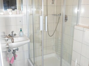 Ein Badezimmer mit Duschkabine, Waschbecken und Spiegel sowie Seifenspender.
