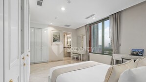 A hotel room with a large bed, a desk with a laptop, a wardrobe, and a view of the city through the window. - Brassia by Kozystay - Thamrin (Jakarta)