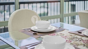 A dining table with a white bowl and spoon, set on a patterned placemat, in a room with a view of buildings through large windows. - Brassia by Kozystay - Thamrin (Jakarta)