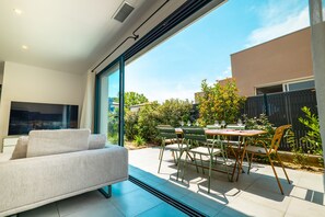 A modern living room with a sofa, a dining table with chairs, and a large window offering a view of the outdoors. - Villa Parenthèse - Elegance & Comfort - Air conditioning (Perpignan)