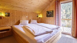 Ein Zimmer in einer Holzhütte mit einem großen Bett, einer Bank und einem Balkon mit Blick auf einen Wald.