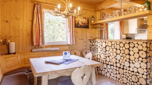 Ein gemütliches Blockhaus-Interieur mit einem Holzesstisch, einer Bank, einem Kronleuchter und einer Holzwand.