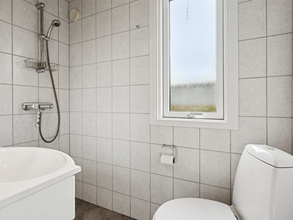 A bathroom with a bathtub, toilet, shower, and a window with a view of a field.