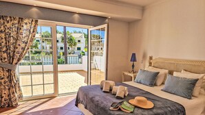 Una habitación de hotel con cama, mesita de noche, lámpara y vistas al exterior.