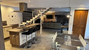 Eine moderne Küche mit einer zentralen Kochinsel, ein Essbereich mit Glastischen und eine Treppe, die zu einem Schlafzimmer führen.
