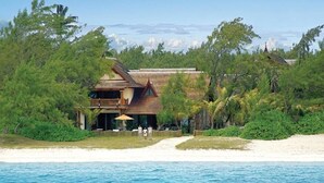 Una proprietà fronte mare con struttura in legno, circondata da vegetazione lussureggiante e una spiaggia sabbiosa.