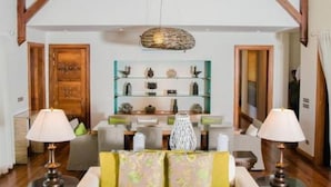 Una stanza spaziosa con soffitto alto, travi in legno, un'elegante libreria centrale in vetro con oggetti decorativi e due lampade sui comodini.