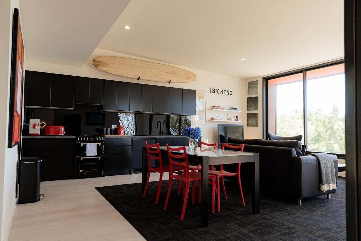 A modern kitchen with black cabinets, a dining area with red chairs, and a large window providing natural light.