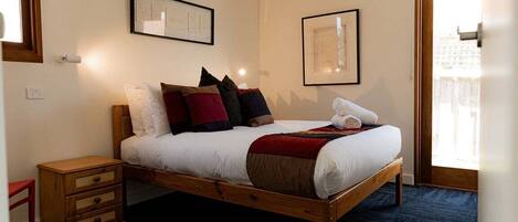 A neatly made bed with a wooden frame, a bedside table with drawers, and two framed pictures on the wall.
