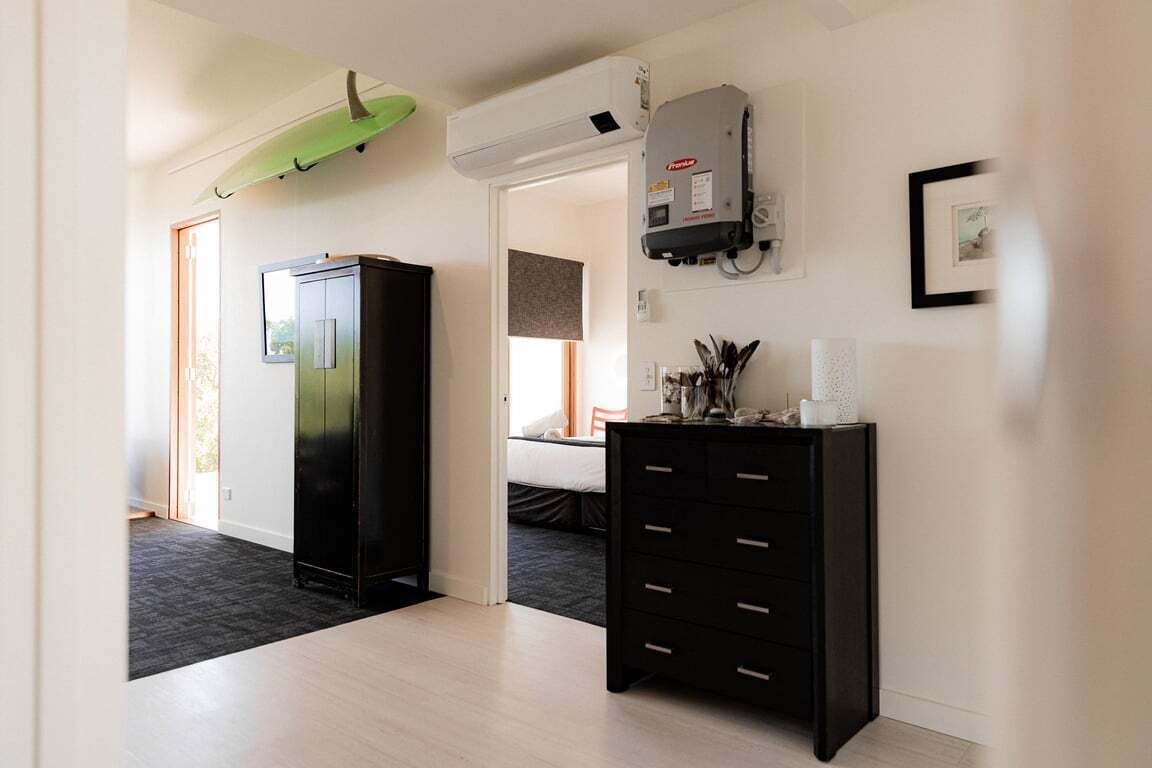A modern hotel room with a black wardrobe, a desk with drawers, a wall-mounted heater, and a framed picture on the wall.