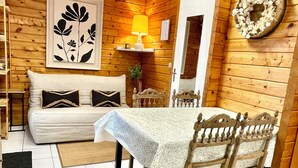 A cozy wooden cabin interior with a sofa, a table with chairs, a lamp, and a framed artwork on the wall.