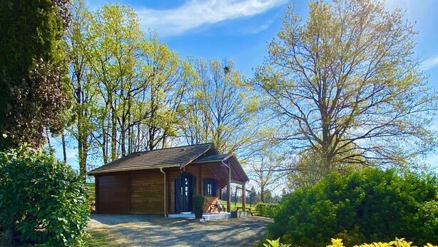 A wooden cabin with a gravel driveway, surrounded by lush greenery and trees.