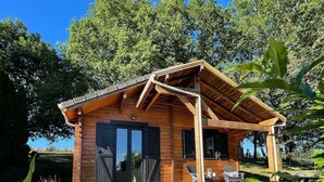 A wooden cabin with a porch, large windows, and a gravel driveway.
