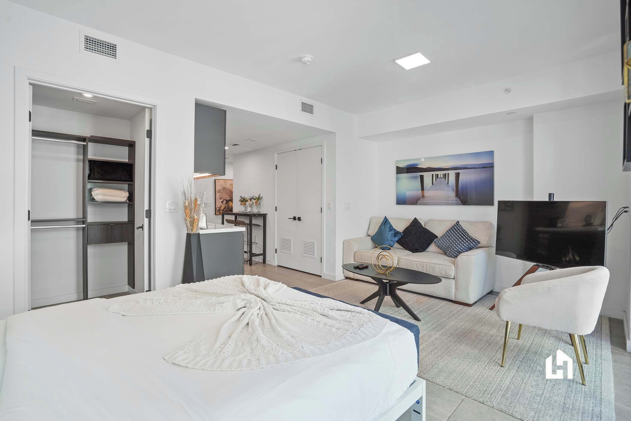 A modern hotel room with a bed, a sofa, a TV, and a desk with a chair.