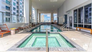 Un área de piscina interior moderna con vistas despejadas al horizonte urbano, múltiples sillones de descanso y un diseño espacioso.