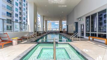 A modern indoor pool area with clear views of the city skyline, multiple lounge chairs, and a spacious design.