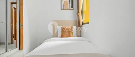 A modern hotel room with a bed, a framed abstract artwork, a window with curtains, and a door leading to another room.