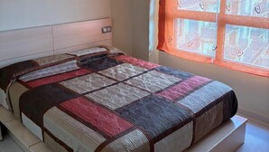 Un dormitorio con cama, ventana con cortinas y una lámpara fijada a la pared.