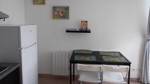 Une petite pièce avec un réfrigérateur blanc, une table avec des chaises et deux tableaux encadrés accrochés au mur.