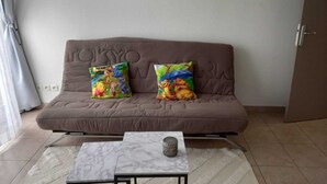 Un salon avec un canapé marron, deux coussins ornés de personnages de dessins animés, une petite table avec un plateau en marbre et un tableau encadré accroché au mur.