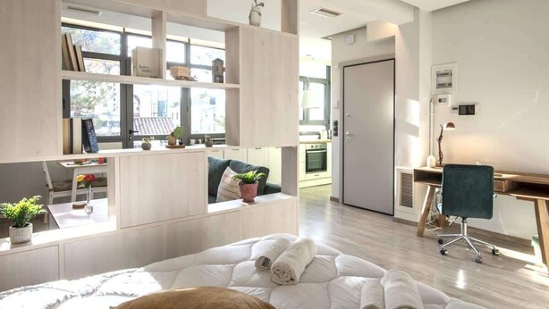 A modern, well-lit room with a bed, a desk, and a shelving unit with books and decorative items. - Luxury Haven in the most ideal area of Athens (Athina)