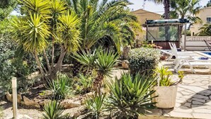 A garden with various plants, a pool area with lounge chairs, and a covered seating area. - Sueño II by Interhome (L'Ametlla de Mar)