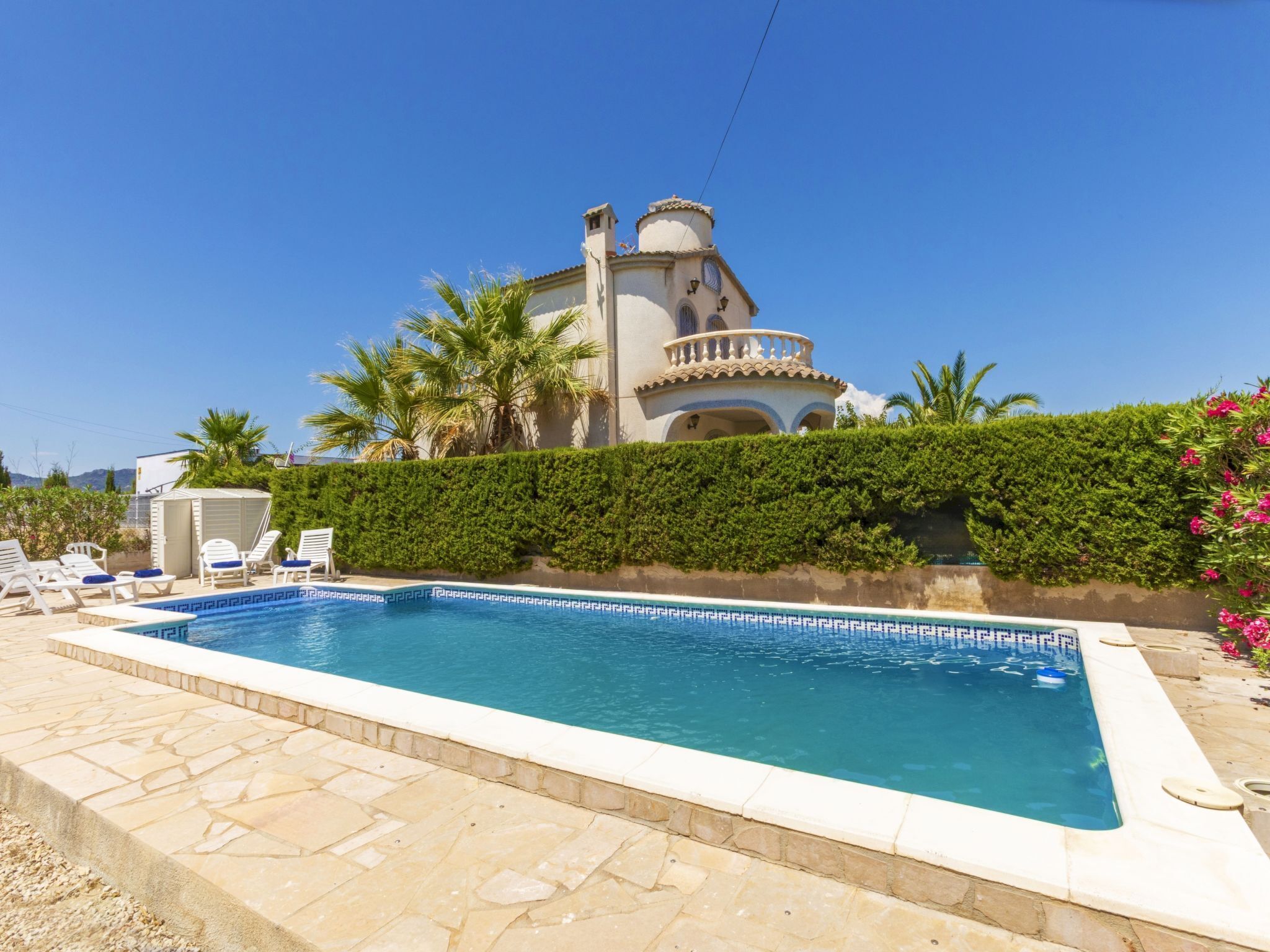 A swimming pool with lounge chairs and a building with a balcony in the background.