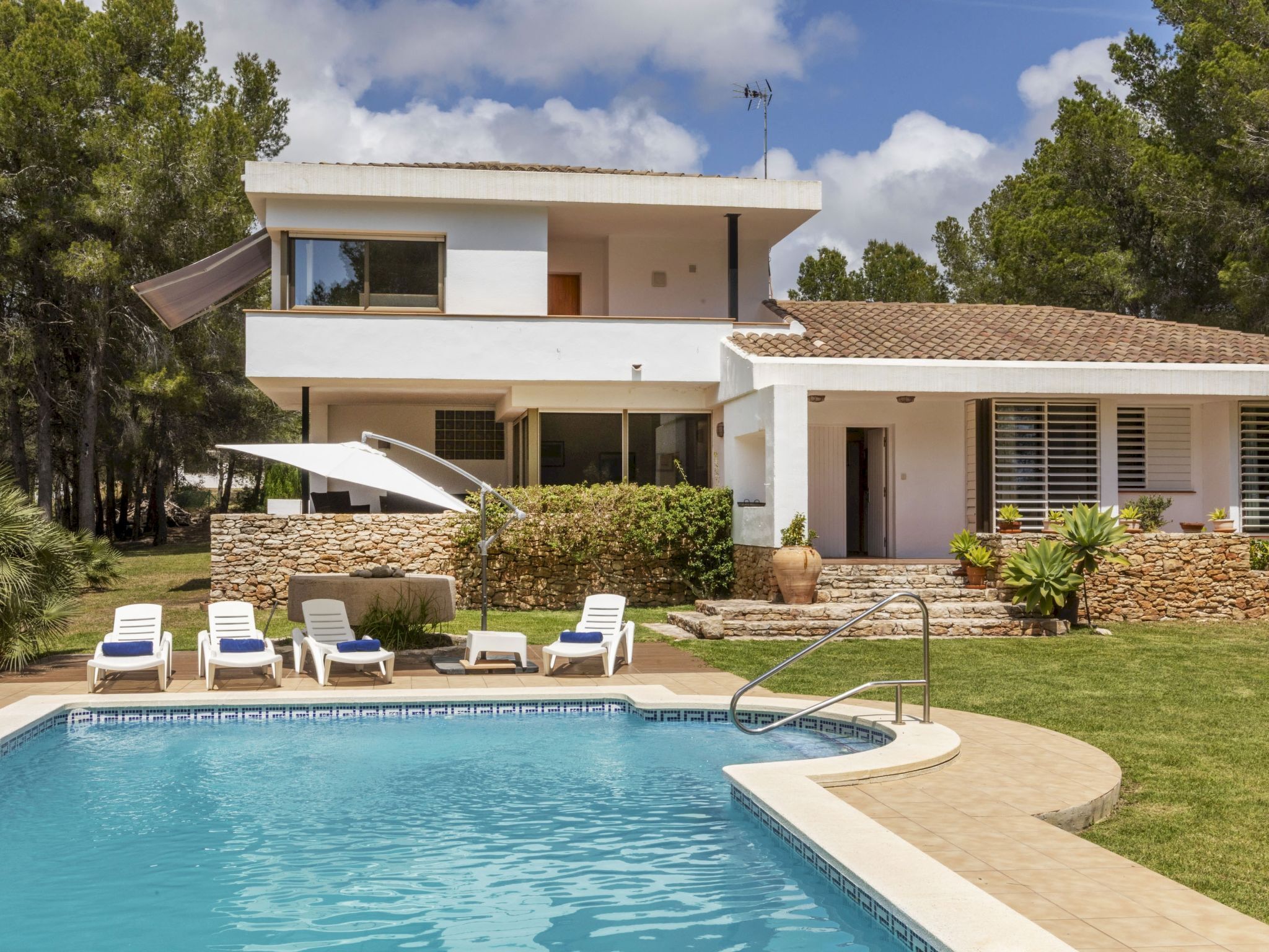 Uma casa moderna de dois andares com piscina, área de estar externa e um muro de pedra.