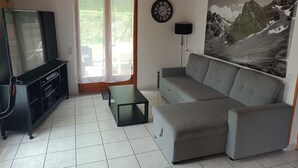 A living room with a sofa, TV, entertainment unit, and a painting. - Chambre et Table d'Hôtes (Campan)
