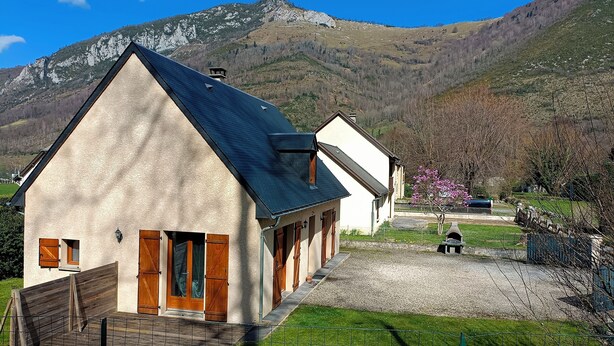 A two-story building with a sloped roof and wooden shutters, located in a rural setting with a mountain backdrop. - Chambre et Table d'Hôtes (Campan)