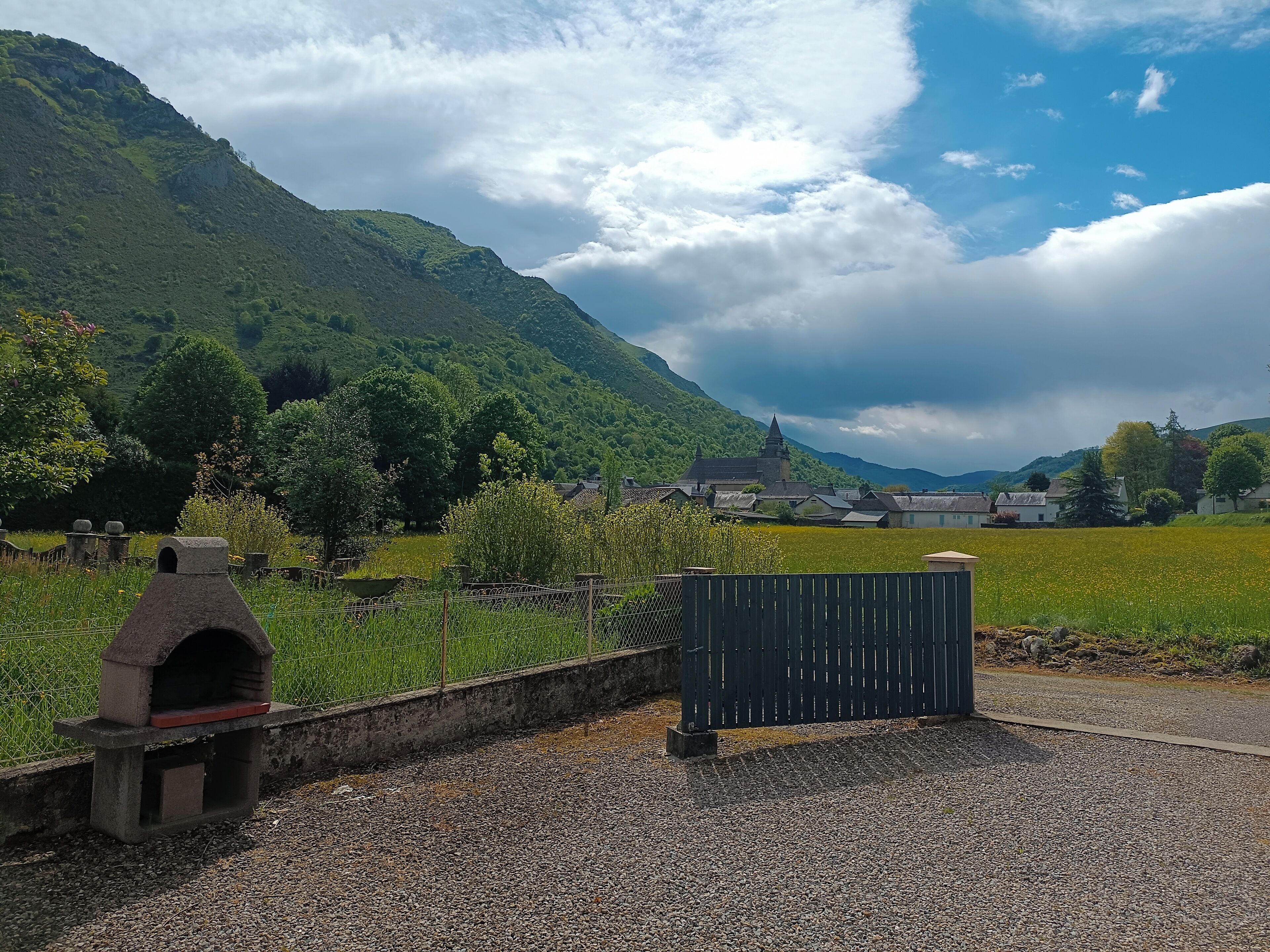 A rural landscape with a stone oven, a wooden fence, and a field of yellow flowers.