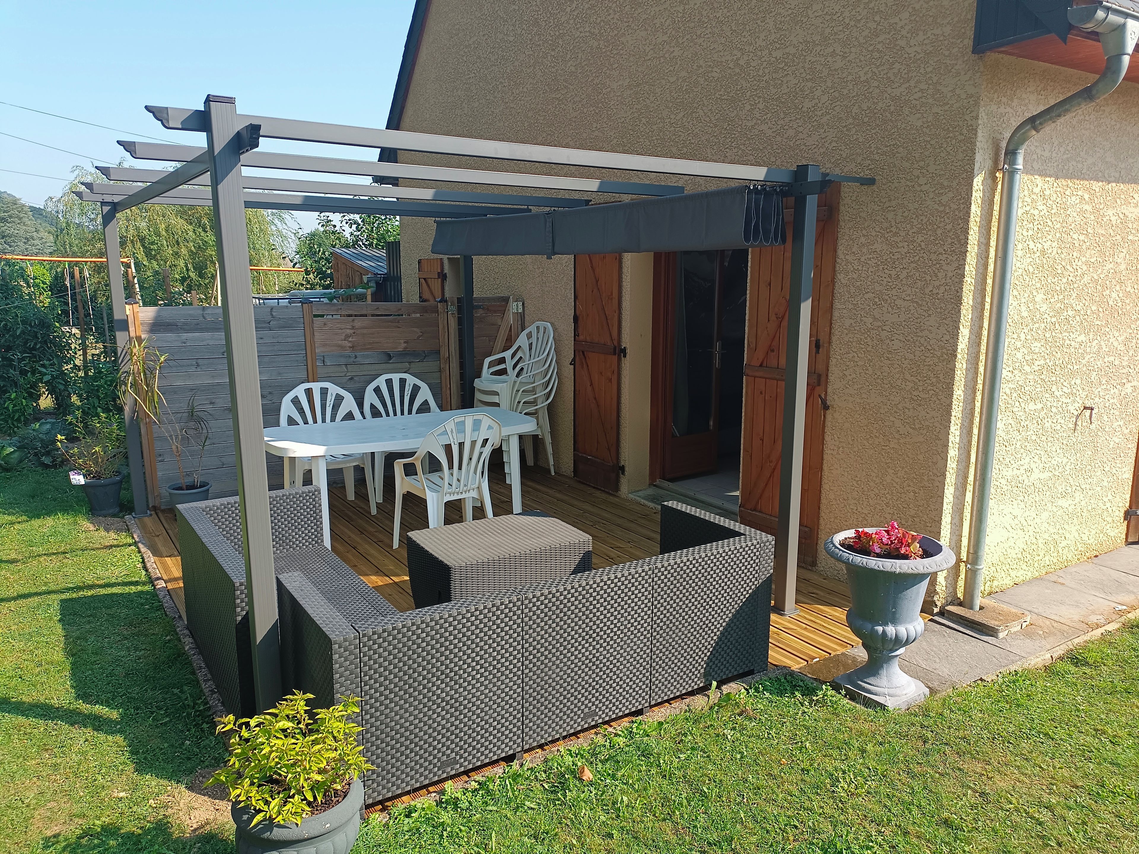 En udendørs terrasse med pergola, et bord med stole og et siddeområde.