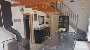 A dining area with a long table, chairs, a stove, a staircase, and a cabinet with glassware. - Chambre et Table d'Hôtes (Campan)