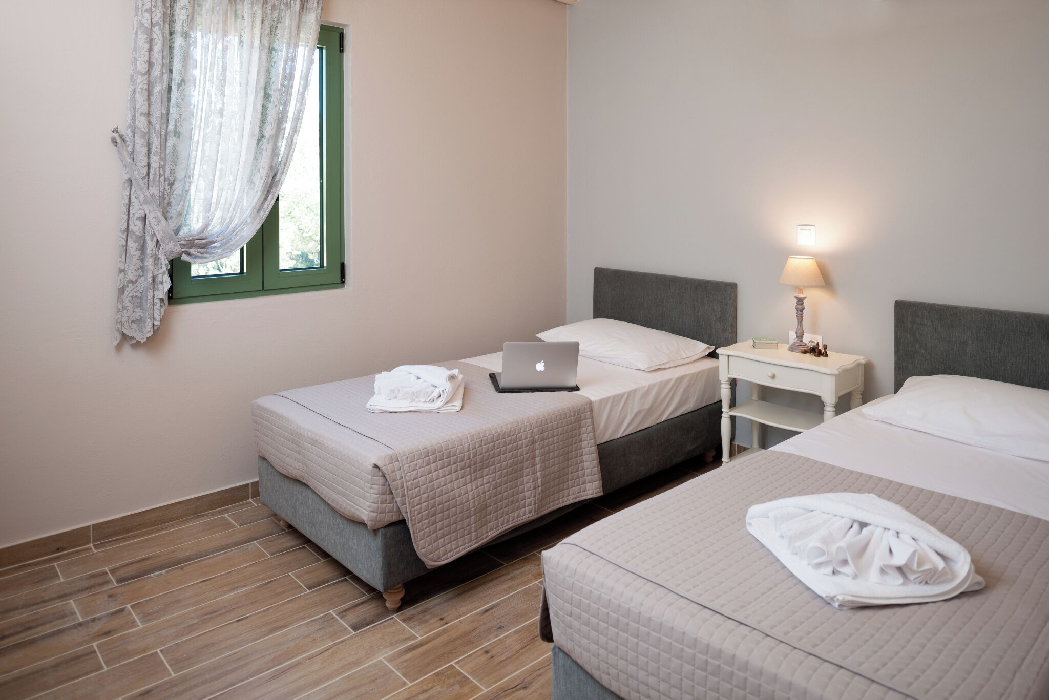 A hotel room with two beds, a laptop on one bed, a lamp on a bedside table, and a window with curtains.