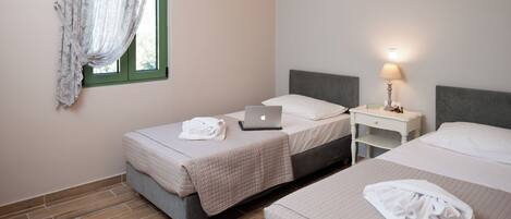 A hotel room with two beds, a laptop on one bed, a lamp on a bedside table, and a window with curtains.