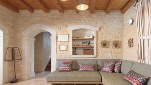 A cozy living room with a stone wall, wooden beams, a sofa with colorful pillows, a wooden table with a bowl, and a staircase leading to another room. - Sarpedon & Rhadamanthus By Forest Villas (Rethymno)