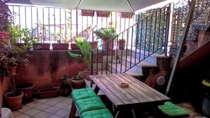 Un espace patio avec une table en bois et des sièges rembourrés de couleur verte, entouré de plantes en pot et d’un escalier en métal.