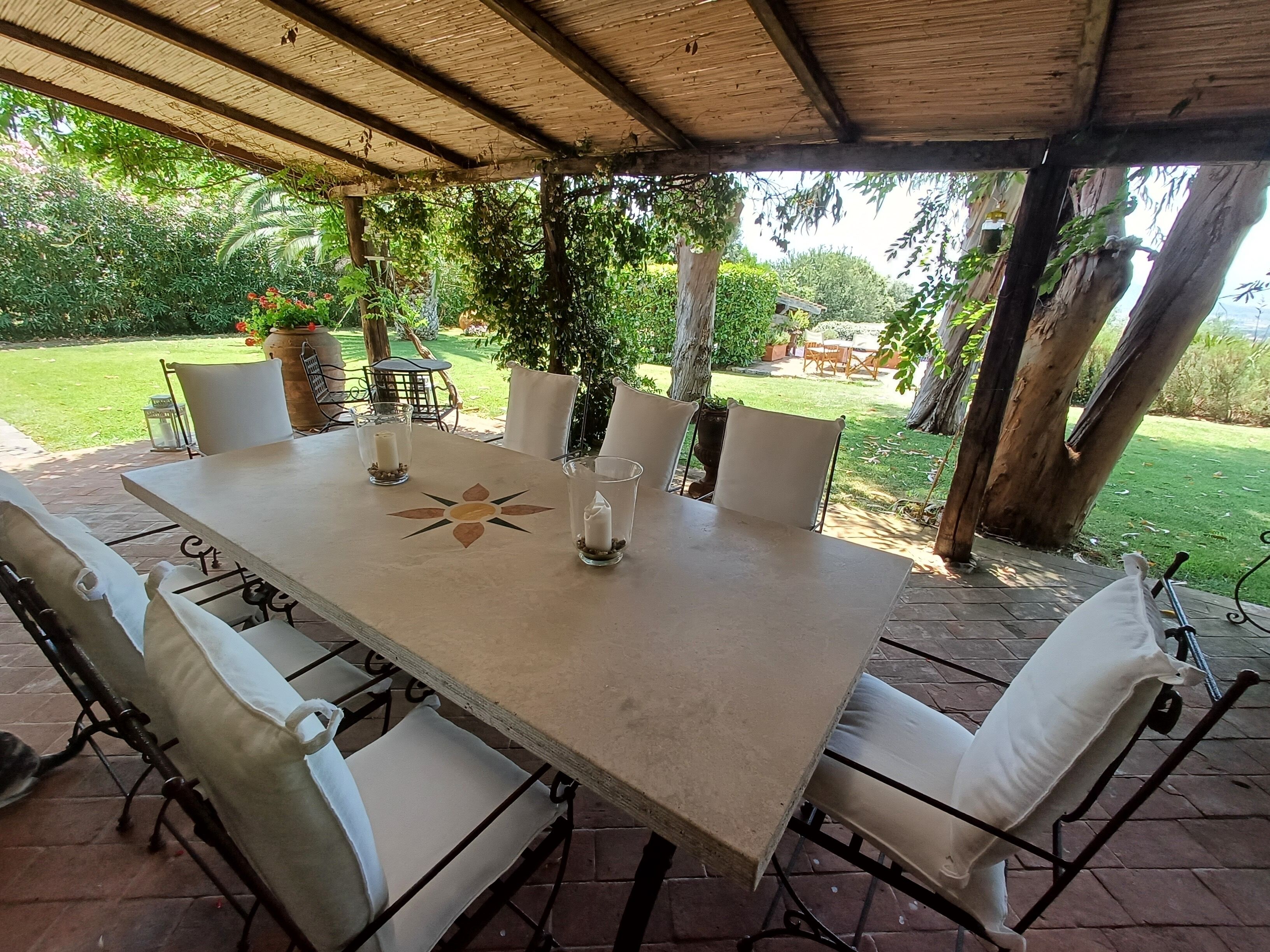 An outdoor patio with a table set for four, surrounded by white cushioned chairs.