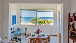 Una habitación con vistas al mar, una mesa de comedor con sillas, una estantería y una ventana con persianas.