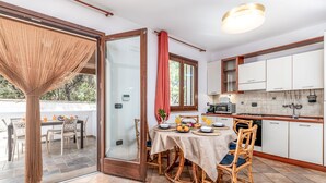 Un comedor con una mesa lista para el desayuno, una cocina con electrodomésticos modernos y un ventanal que da a una zona de estar exterior.