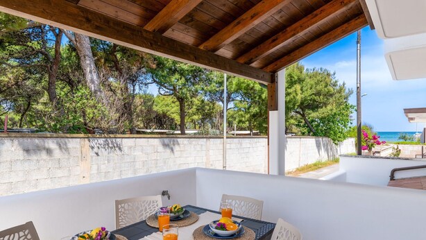 Un área de comedor al aire libre con una mesa lista para el desayuno, rodeada de árboles y vistas al mar.
