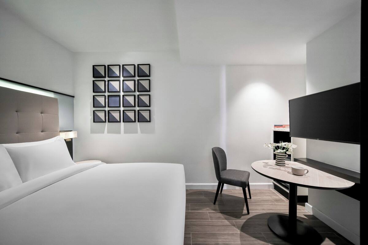 Une chambre d’hôtel moderne avec un grand lit, une petite table sur laquelle se trouvent une tasse et des fleurs, une chaise et un téléviseur fixé au mur.