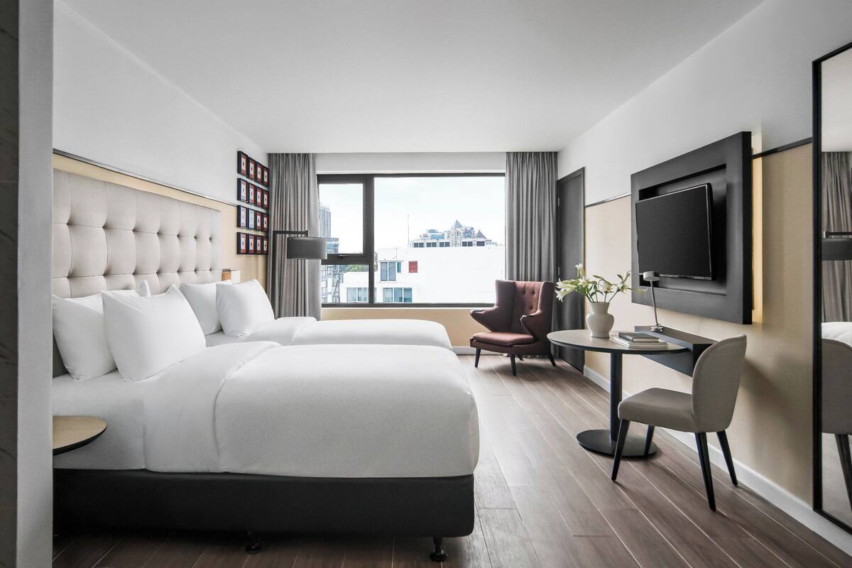 Une chambre d’hôtel moderne dotée d’un grand lit, d’un bureau, d’une chaise, d’une télévision et offrant une vue sur la ville.
