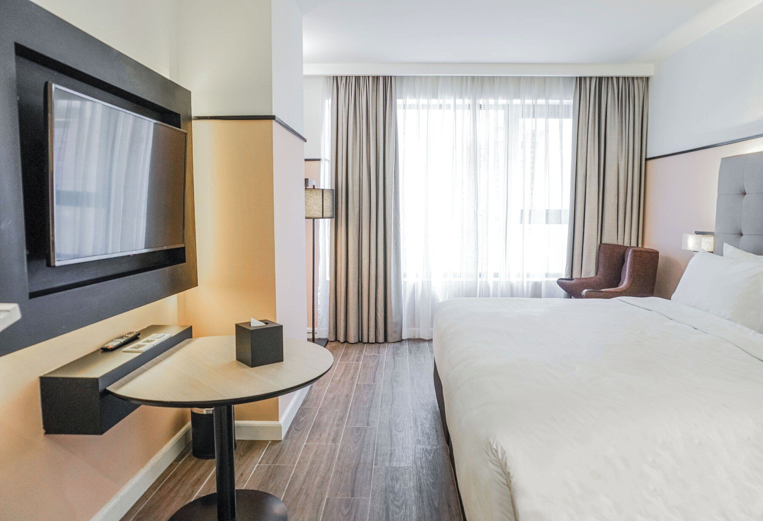 A hotel room with a large bed, a TV mounted on the wall, a small table, and a chair.